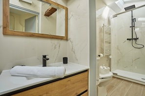 Ein Badezimmer mit weißem Waschbecken, Holz-Badmöbeln, einem Spiegel mit Holzrahmen, einer Dusche mit Glastür und einer Toilette.