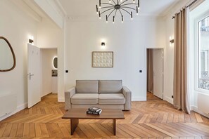 A modern living room with a sofa, a coffee table with books, a decorative wall piece, and a ceiling light fixture. - Elegant Renovated Apartment - Center of Paris (Paris)