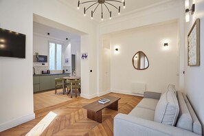 A modern living room with a sofa, a coffee table, and a dining area with chairs and a table. - Elegant Renovated Apartment - Center of Paris (Paris)