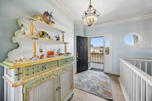Ein Flur mit einem dekorativen Schrank, einer Chandelieber, einer zur Außenwelt führenden Tür und Blick ins Freie.