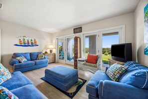 Ein Wohnzimmer mit blauem Sofagarnitur, einem Fernseher und einem großen Fenster.