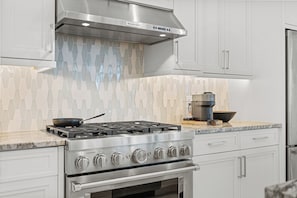 A kitchen with a gas stove, oven, stainless steel cabinets, and a backsplash with a geometric pattern. - Luxe Waterfront 4 Bed Escape | Near Beach (Marco Island)