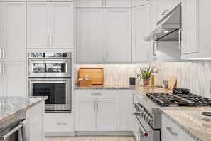 A modern kitchen with stainless steel appliances, white cabinetry, a marble countertop, and a wooden cutting board. - Luxe Waterfront 4 Bed Escape | Near Beach (Marco Island)