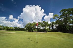 Un campo da golf con una bandiera, bunker di sabbia e cielo sereno.
