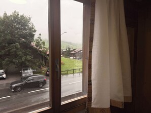 Ein Fenster mit Blick auf eine Straße und Häuser, teilweise zurückgezogene Vorhänge und ein Türrahmen.