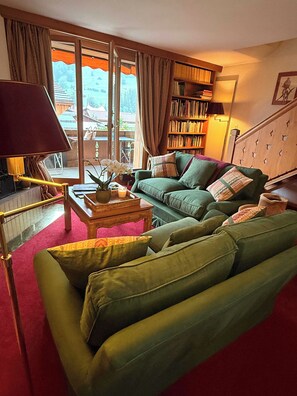 Ein Wohnzimmer mit einem grünen Sofa, einem Holztisch und einem Bücherregal.