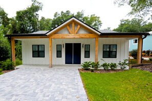 A modern two-story house with a symmetrical facade, a central entrance with a dark-colored door, and a covered porch area. - Downtown Bungalow ~ 3BR 3.5BA Home, New Build, Private Yard (Fernandina Beach)