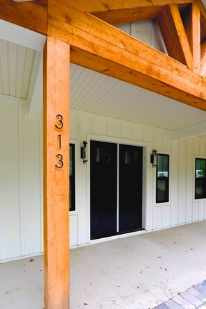 A building entrance with a wooden beam structure, two black doors, and the number 313 on a wooden post. - Downtown Bungalow ~ 3BR 3.5BA Home, New Build, Private Yard (Fernandina Beach)