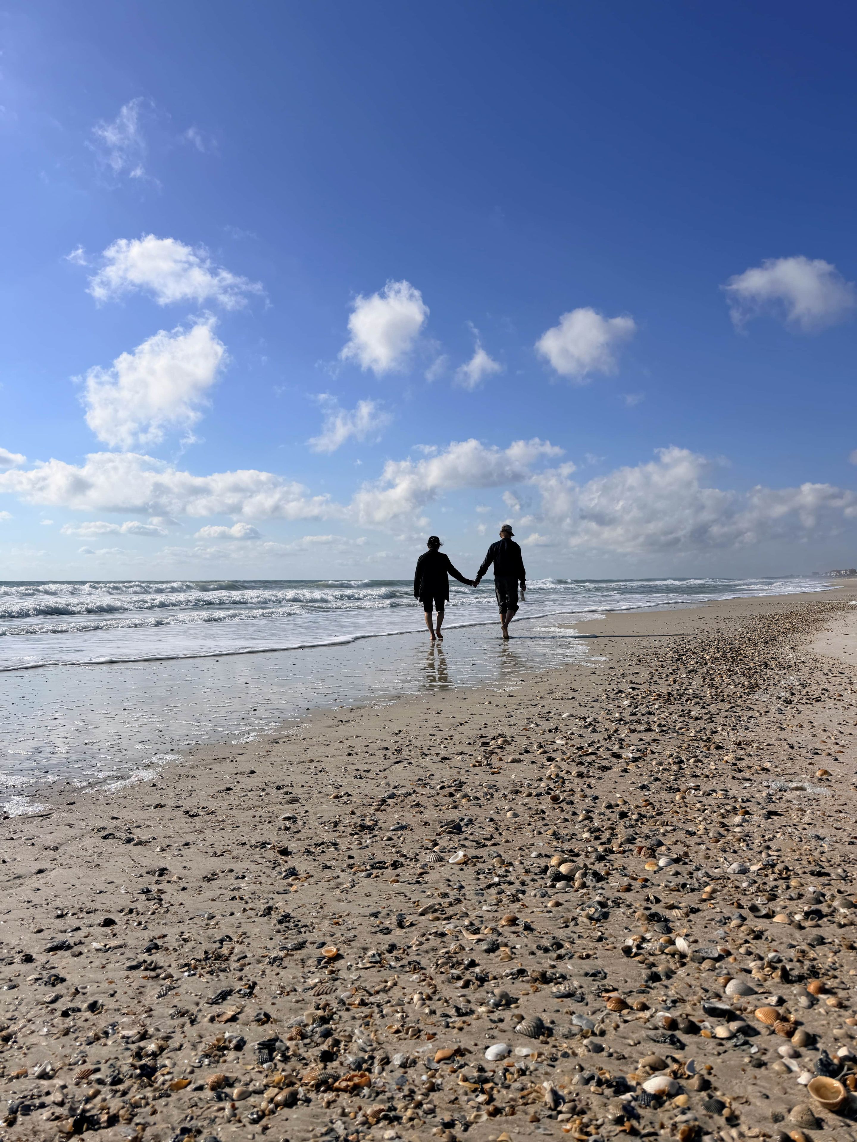 A beach with pebbles and shells, and two people walking along the shore.