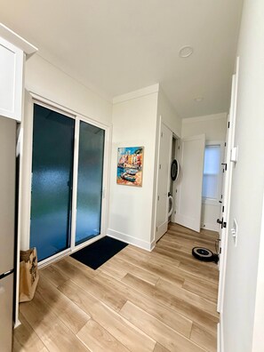 A hallway with a sliding glass door, a painting of a coastal scene, a washing machine, and a vacuum cleaner. - Downtown Bungalow ~ 3BR 3.5BA Home, New Build, Private Yard (Fernandina Beach)