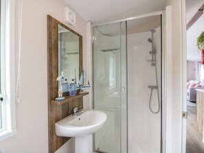 A bathroom with a glass-enclosed shower, a white sink, and a wooden vanity with a mirror. - Frontline Sea View : P1 Whilk Meadow Caravan Park (Girvan)