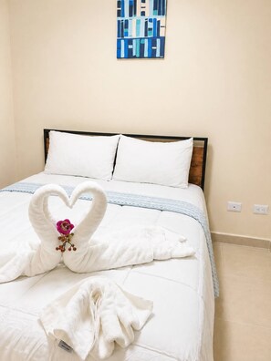 Ein Hotelzimmer mit einem Bett, weißen Kissen, einer blau-weißen Streifendecke und einer herzförmigen Handtuchdeko mit einer Blume.