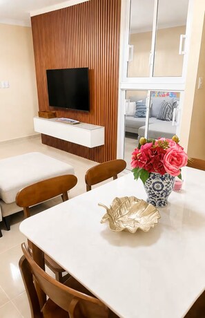 Ein modernes Wohnzimmer mit einem flachbildfernseher an einer Holzwand, einem Esstisch mit Stühlen und einer Blumenvase.