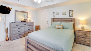 Un dormitorio con cama, cómoda, mesita de noche, lámpara, espejo y televisor.