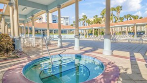 Ein Poolbereich mit Whirlpool, Liegestühlen und einer überdachten Terrasse mit Säulen.