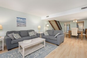 Ein Wohnzimmer mit zwei grauen Sofas, einem Couchtisch, einem gemusterten Teppich und einer Treppe zu einem anderen Raum.