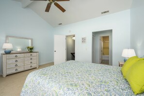 Ein Schlafzimmer mit Bett, Schminktisch, Spiegel, Deckenventilator und einer Badezimmertür.
