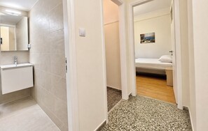 A hallway leading to a bathroom with a tiled floor, a sink, and a bed with a white headboard. - Stylish Couples Hideaway in Pangrati by ΜΡS (Athina)