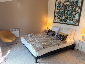 A bedroom with a bed, a chair, a painting, and a lamp. - A large, renovated house, just a stone's throw from downtown! (La Rochelle)