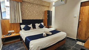 A hotel room with a bed, bedside table, and a wall-mounted air conditioner. - Hotel Alfa View (Ahmedabad)