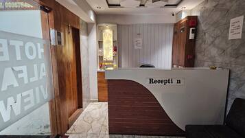 Balcão de recepção com placa indicando 'Recepção' e sinalização com horários de check-in e check-out.