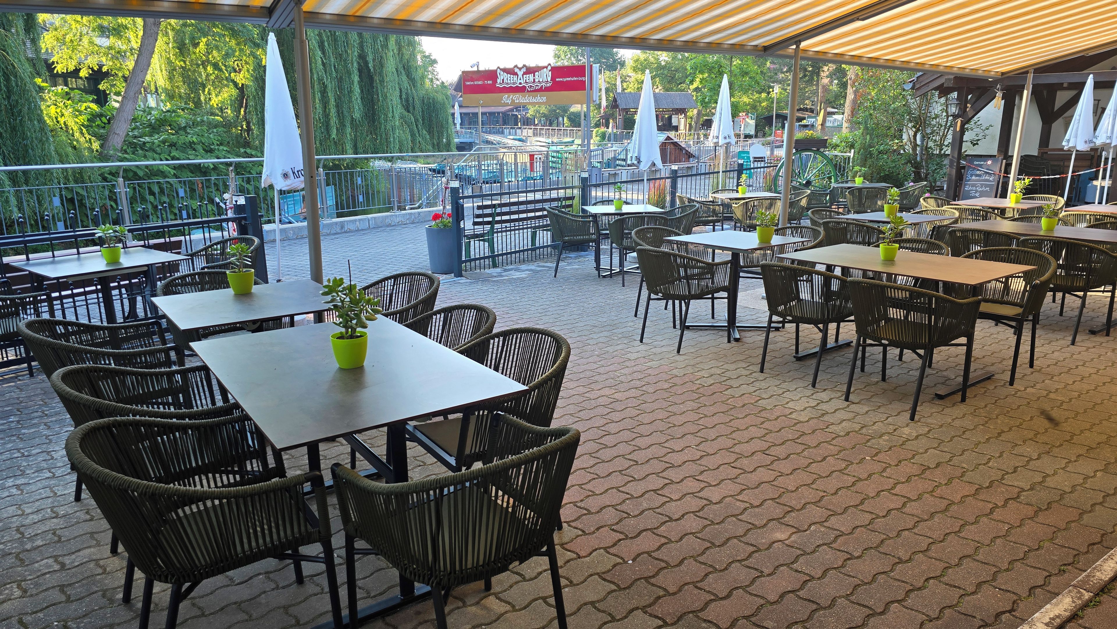 Un área de café al aire libre con mesas y sillas, rodeada por una valla y árboles.