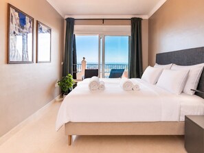 Ein Hotelzimmer mit einem großen Bett, Meerblick und einem Balkon mit einem Stuhl.