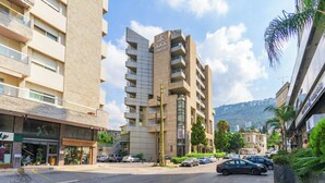 A multi-story building with balconies, a sign for 'AAA COMFORT', and a street with parked cars and greenery. - Maven Studio & Balcony in Jounieh (Jounieh)