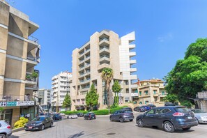 Un edificio de varios pisos con balcones, un estacionamiento con coches y zonas verdes.