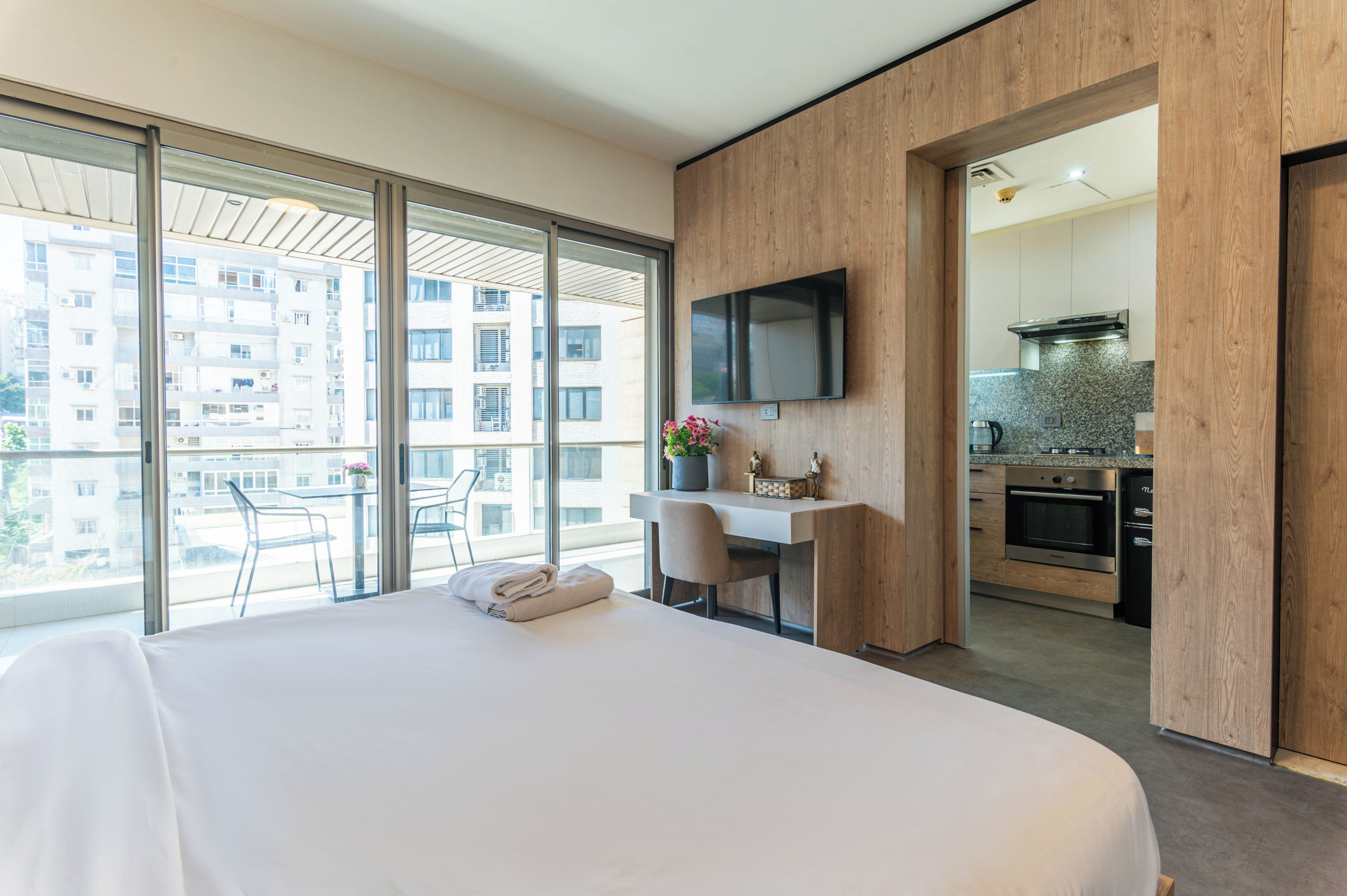 Een hotelkamer met een groot bed, een bureau, een flatscreen-tv en een stadszicht door grote ramen.