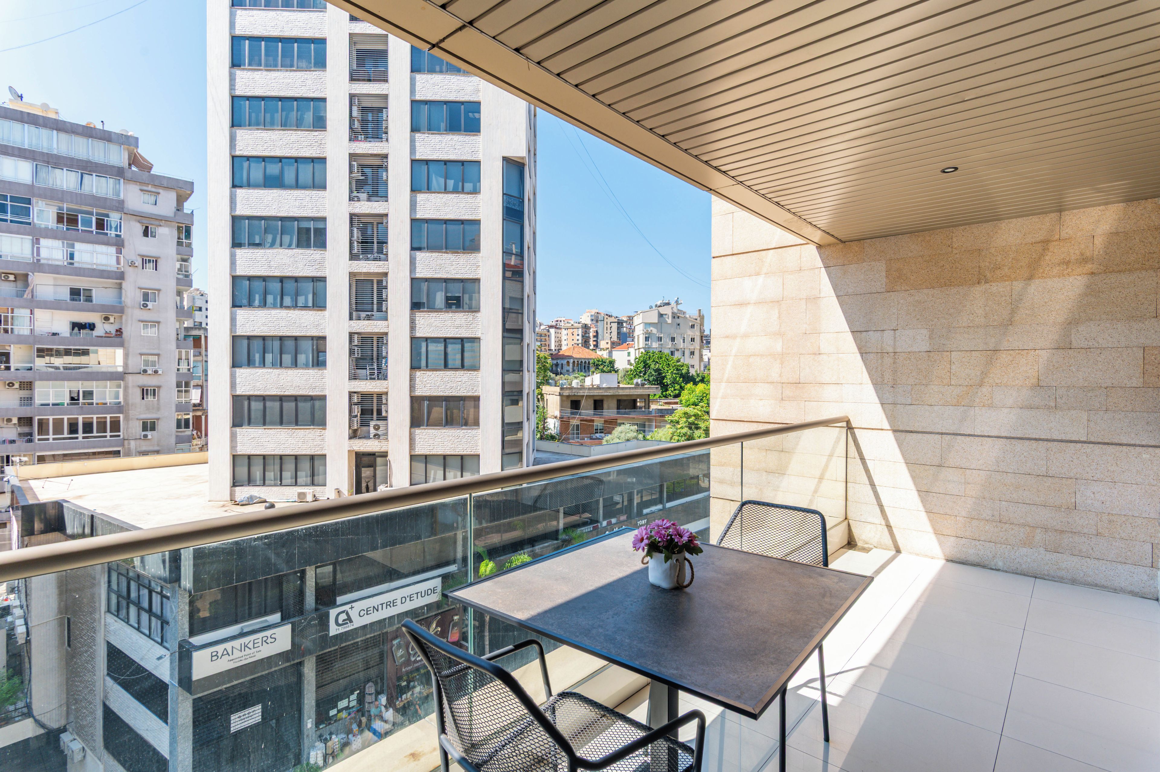 A balcony with a table and chairs, overlooking a cityscape with modern buildings.