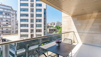 A balcony with a table and chairs, overlooking a cityscape with modern buildings.