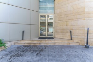 Entrada de edificio con puerta de vidrio, un poste de metal y una zona pavimentada con un desagüe.