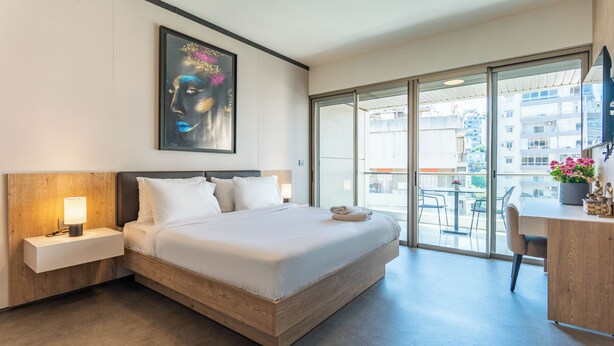 A hotel room with a large bed, a bedside table with a lamp, a painting on the wall, and a view of the city through the balcony doors. - Maven Studio & Balcony in Jounieh (Jounieh)