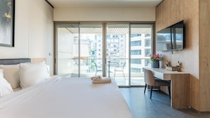 A modern hotel room with a large bed, a desk, a chair, a TV, and a balcony with a view of the city. - Maven Studio & Balcony in Jounieh (Jounieh)
