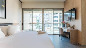 A modern hotel room with a large bed, a desk, a chair, a TV, and a balcony with a view of the city.