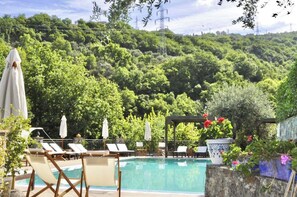 A pool area with lounge chairs and umbrellas, surrounded by lush greenery and a hill in the background. - Farmhouse with panoramic swimming pool in Gioiosa Marea (Gioiosa Marea)