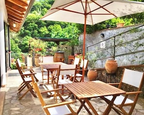 An outdoor patio with wooden tables and chairs, a large umbrella, and potted plants. - Farmhouse with panoramic swimming pool in Gioiosa Marea (Gioiosa Marea)