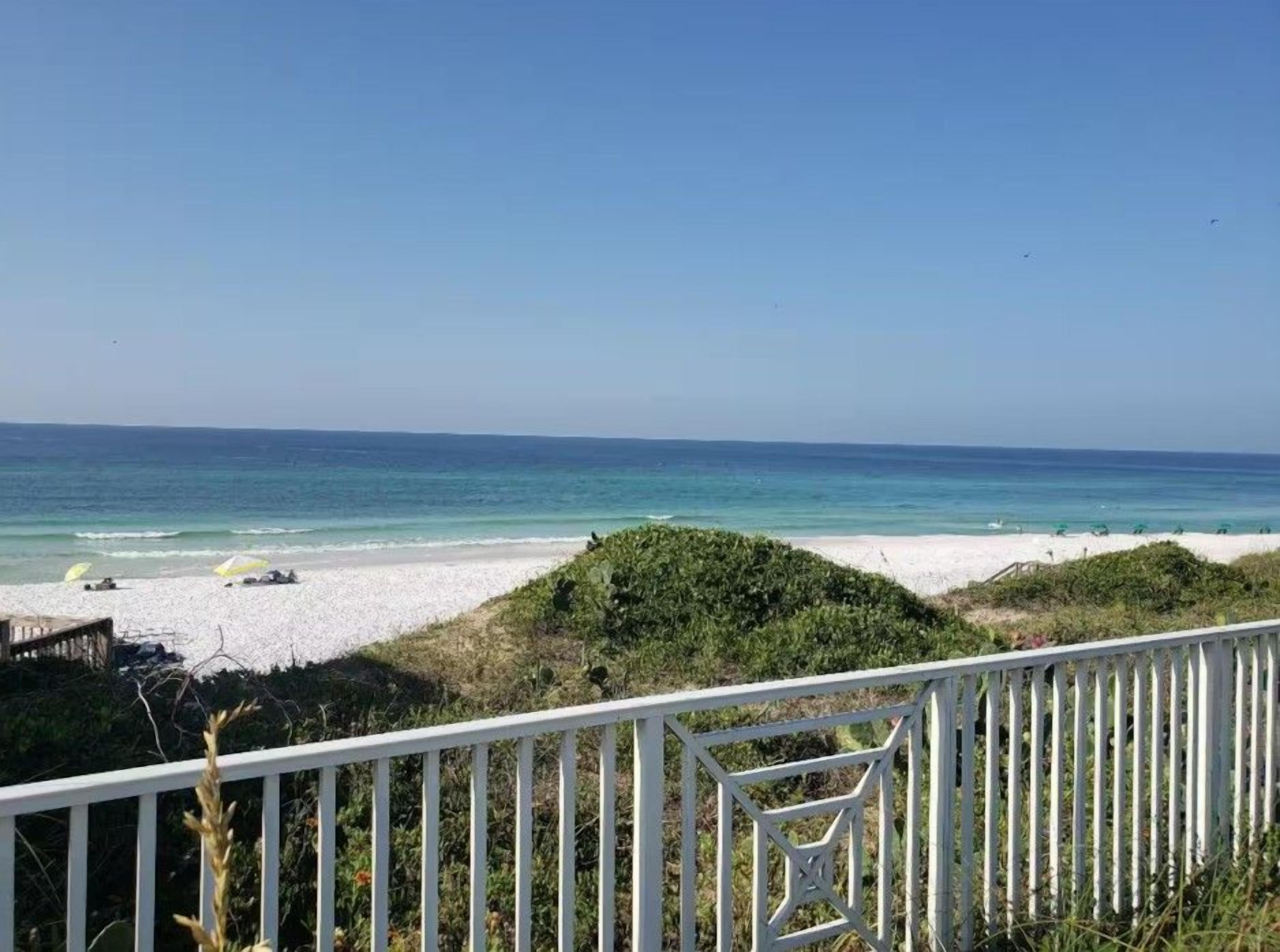 Vista de playa con una cerca blanca al frente, una playa arenosa y el océano.