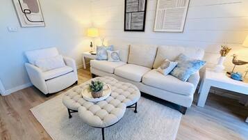 Una sala de estar con un sofá, un sillón, un reposapiés y una mesa de centro.
