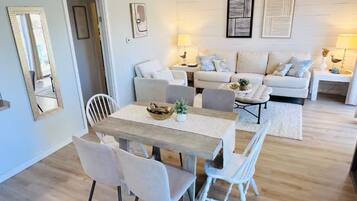 Una sala de estar con un juego de sofá, una mesa de comedor con sillas, un ventilador de techo y decoración en la pared.