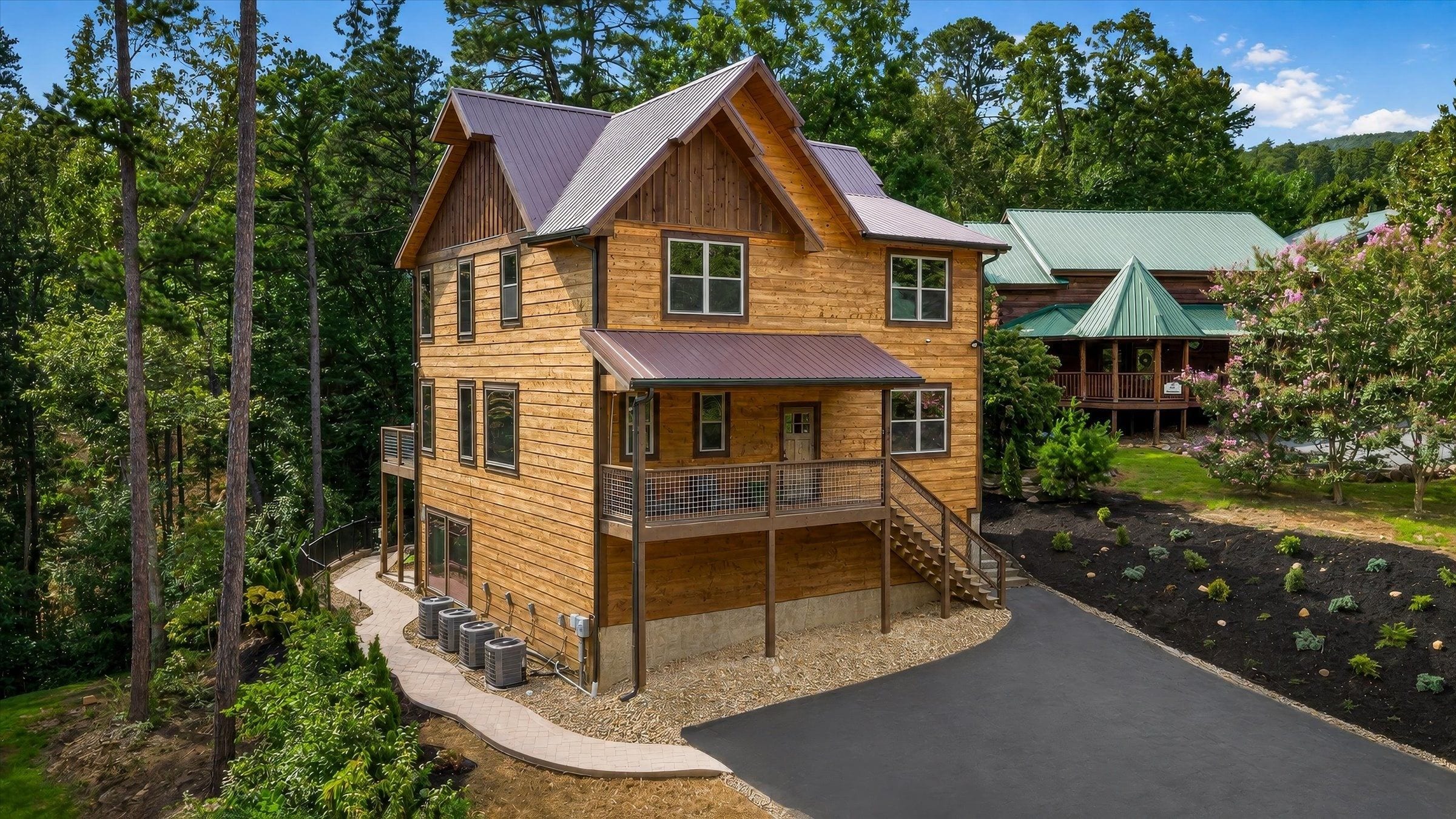 A two-story wooden cabin with a balcony, surrounded by a landscaped garden and trees.