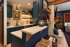 A modern kitchen with a stone wall, wooden cabinets, and a built-in island. - Pinecone Cottage 3 Bedroom Cabin (Leavenworth)