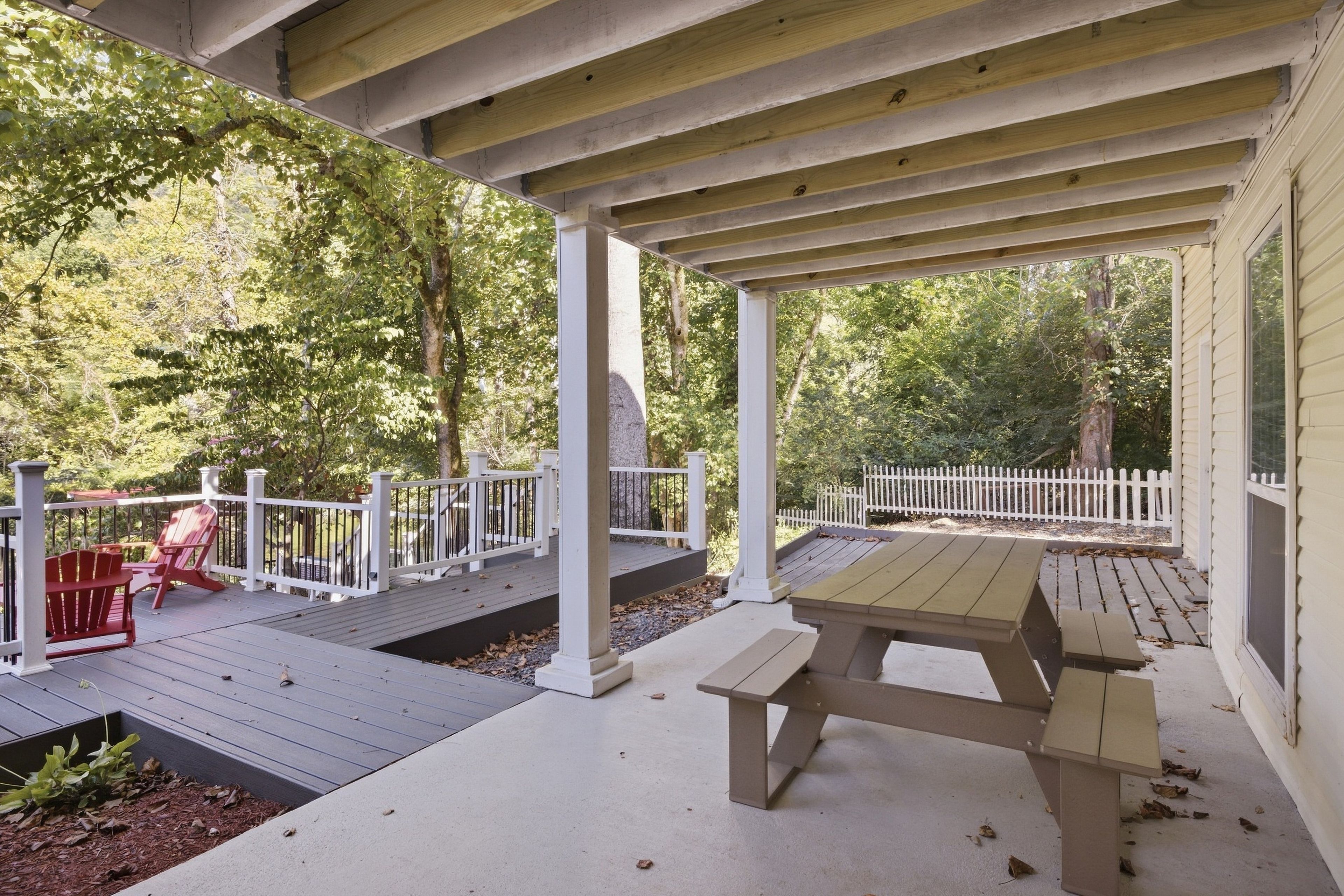 A covered outdoor deck with a picnic table and red Adirondack chairs.