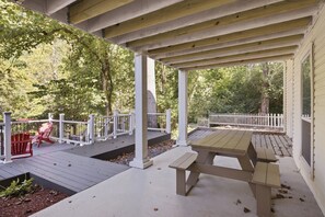 A covered outdoor deck with a picnic table and red Adirondack chairs. - Little River Lodge 5 Bedroom Cabin (Sevierville)