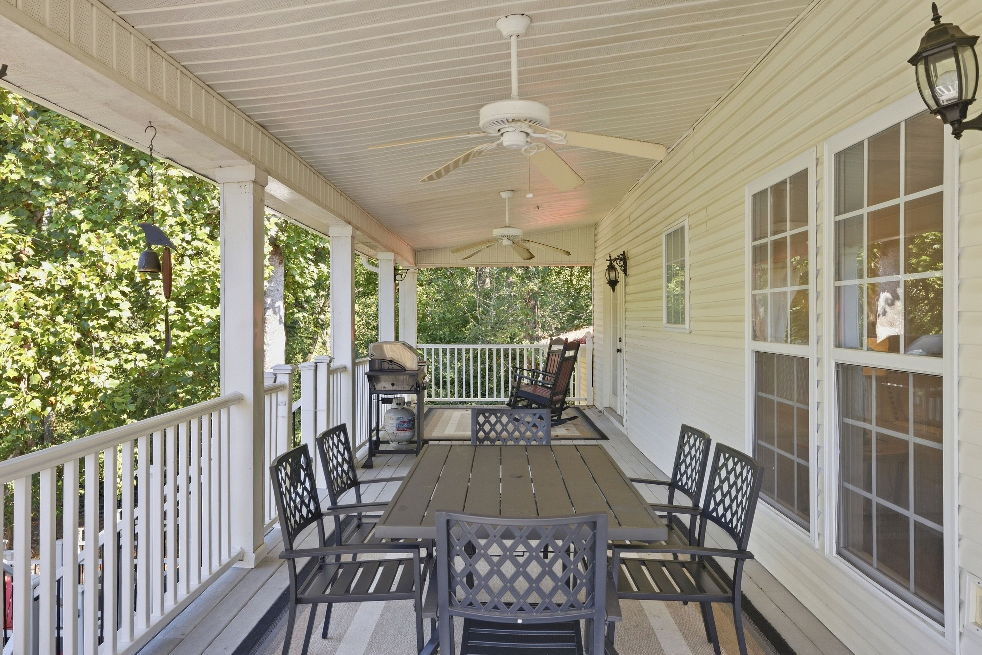 A covered porch with a table and chairs, a grill, and a view of trees.