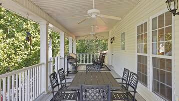 A covered porch with a table and chairs, a grill, and a view of trees.