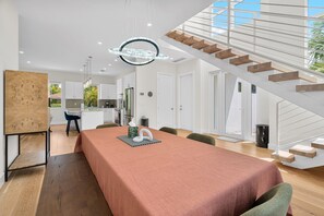 A modern kitchen with white cabinets, a dining area with a table set for two, and a staircase with wooden steps. - Paradise Grove 3 Bedroom Home (Sarasota)
