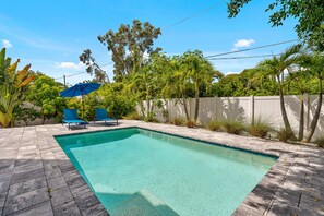A swimming pool with two blue lounge chairs and a blue umbrella. - Paradise Grove 3 Bedroom Home (Sarasota)