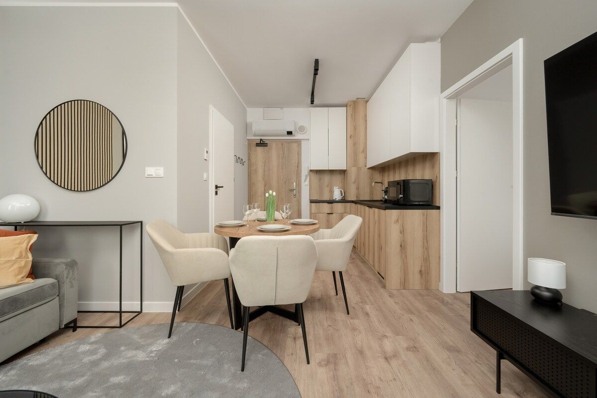 Un salon moderne avec un canapé gris, une table basse ronde et un coin repas comprenant une table et des chaises en bois.